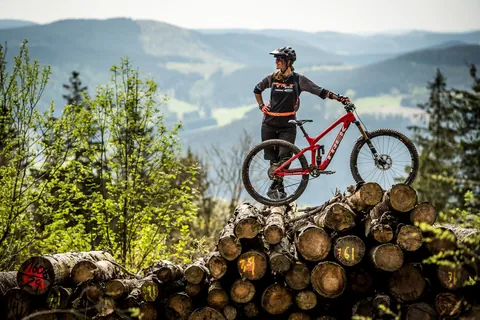 Mountainbiker auf einem Holzstapel vor dem Sauerland-Panorama
