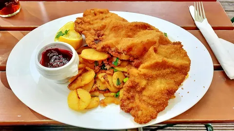 Paniertes Schnitzel mit Bratkartoffeln, Zitrone und Preiselbeeren auf einem weißen Teller