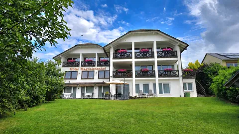 Hotel Magdalenenhof im Sommer: weißes Haus mit Holzbalkonen über einer großen Wiese